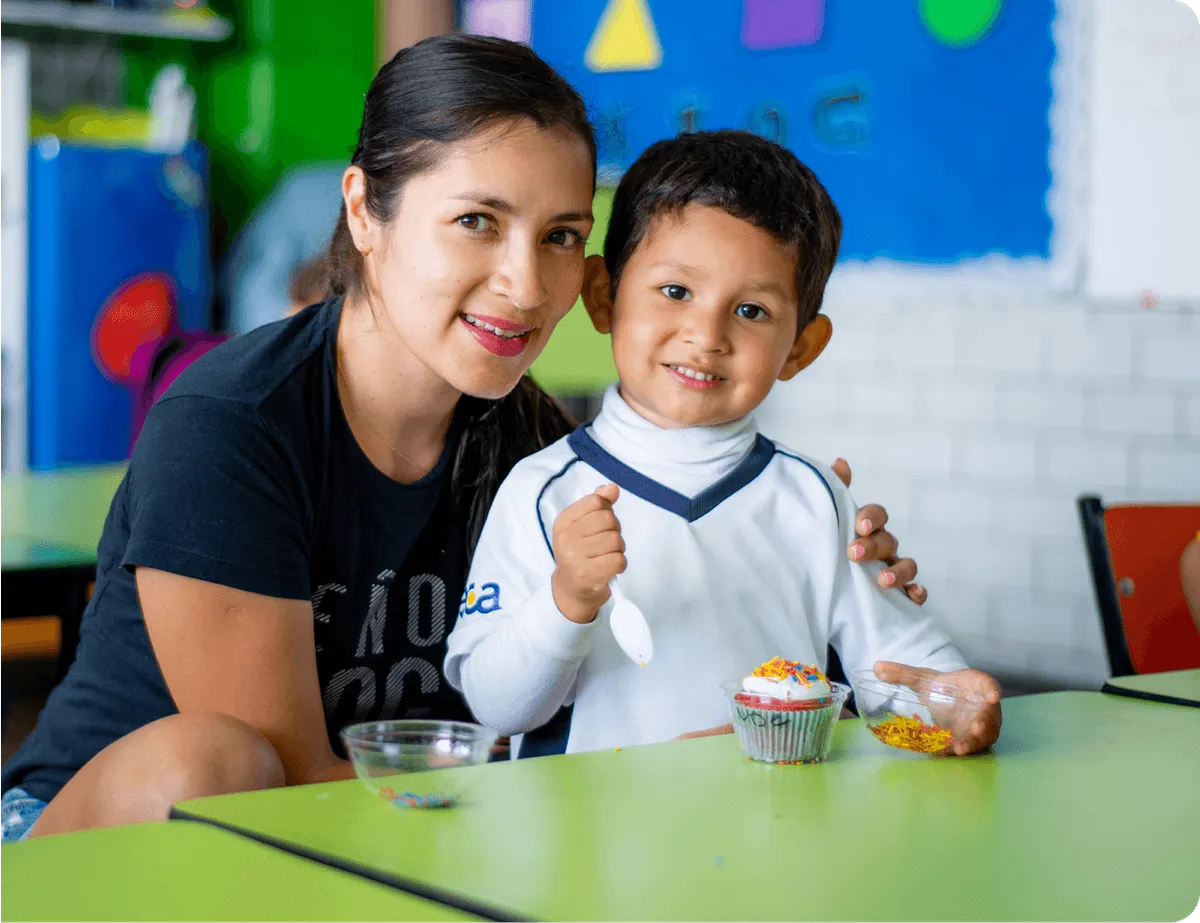 Maestra con una niña de preescolar en una mesa, compartiendo un momento de comida