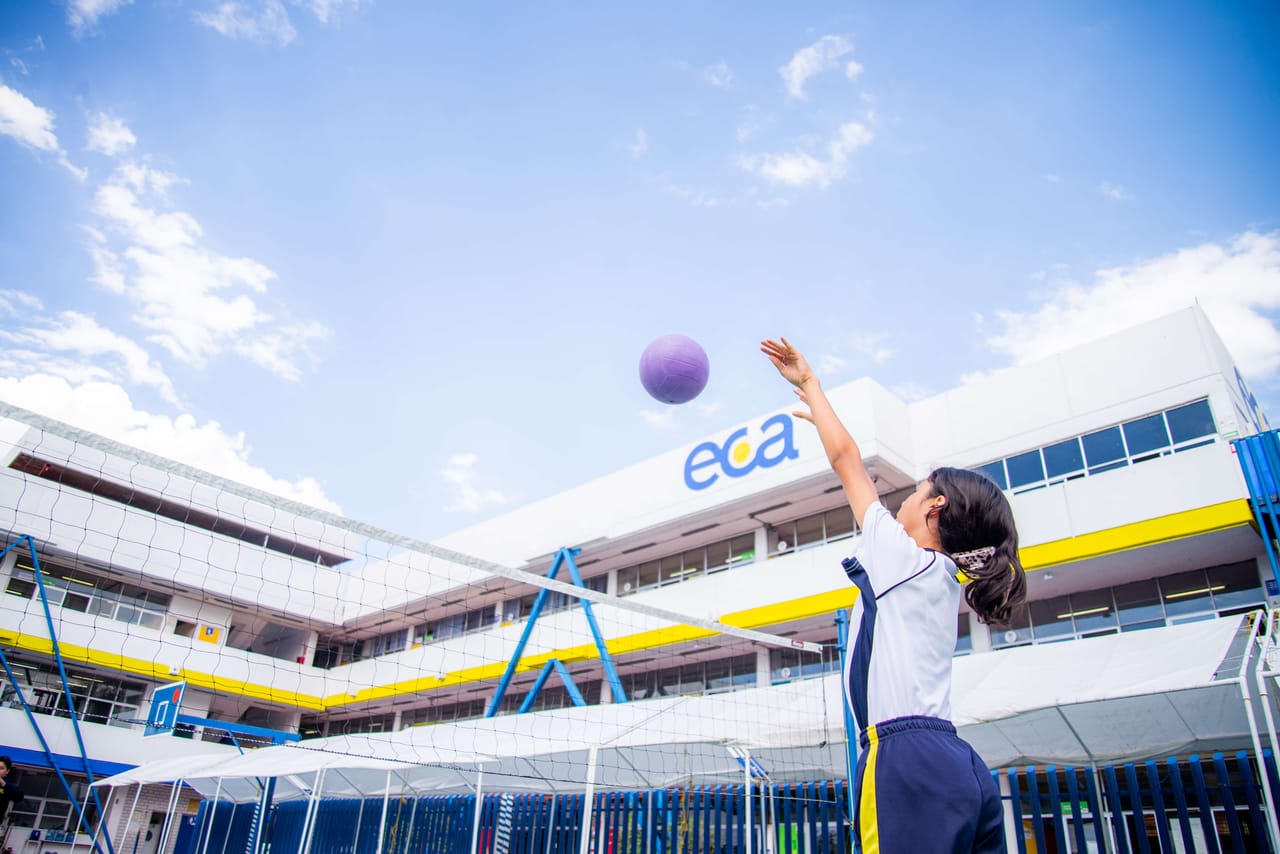 Una alumna lanza una pelota frente al edificio del colegio con el logotipo ECA