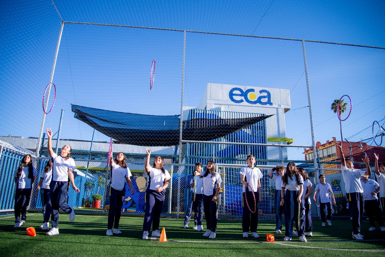 Alumnas hacen ejercicio en la cancha de pasto junto a un letrero de ECA