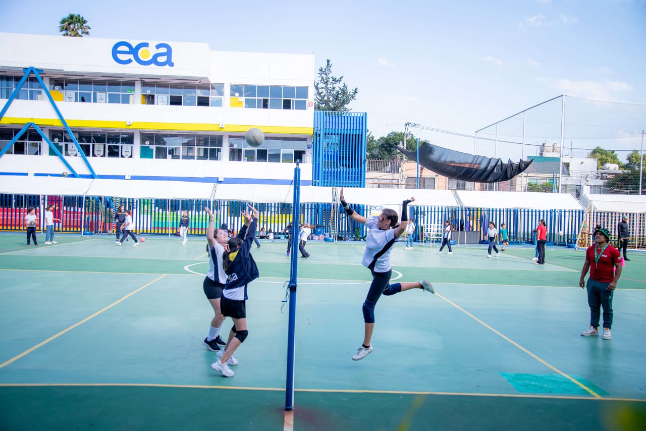Alumnas juegan en la cancha con el edificio ECA detrás, en un día soleado