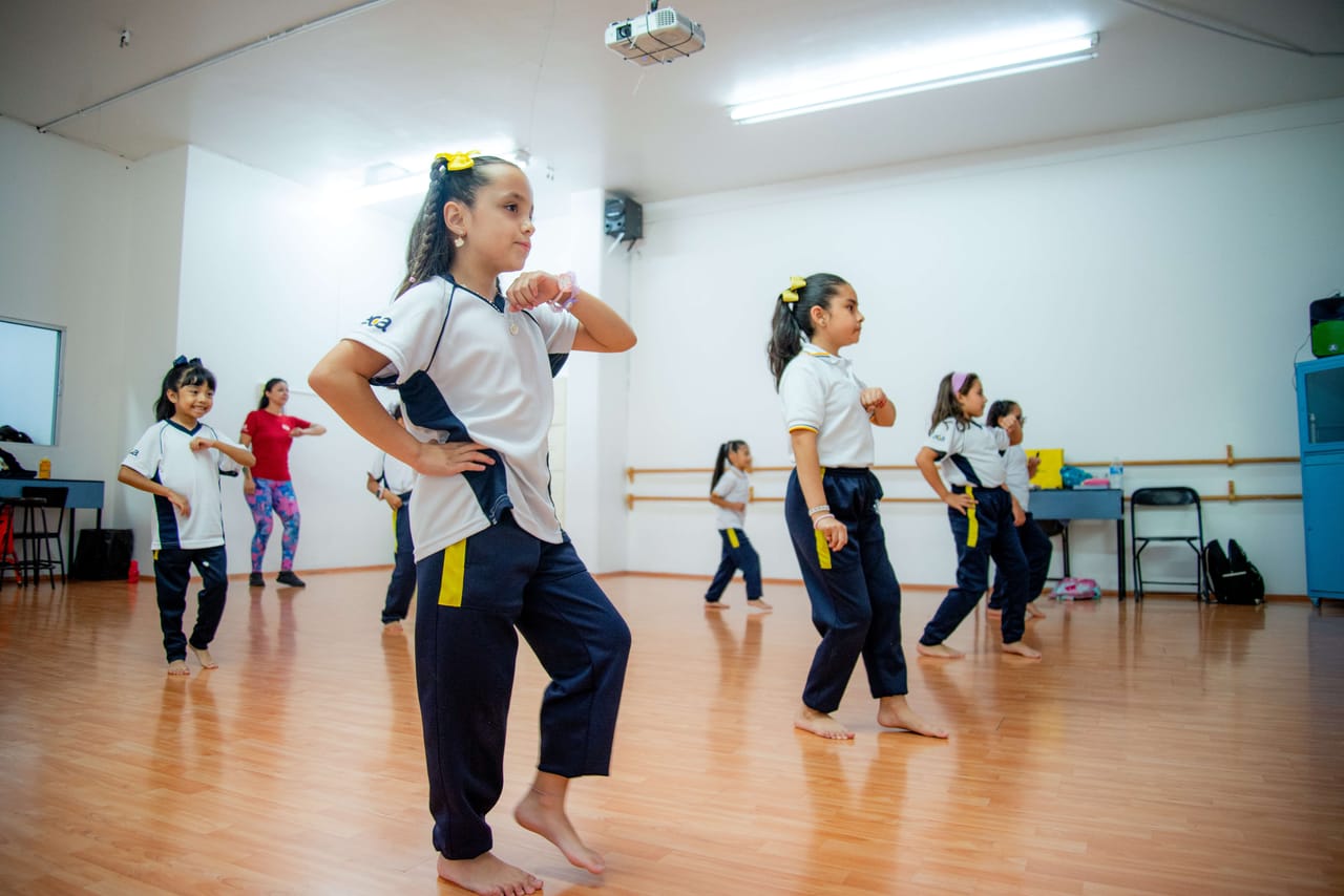 Niñas de uniforme blanco y pantalón marino bailan en el salón de danza